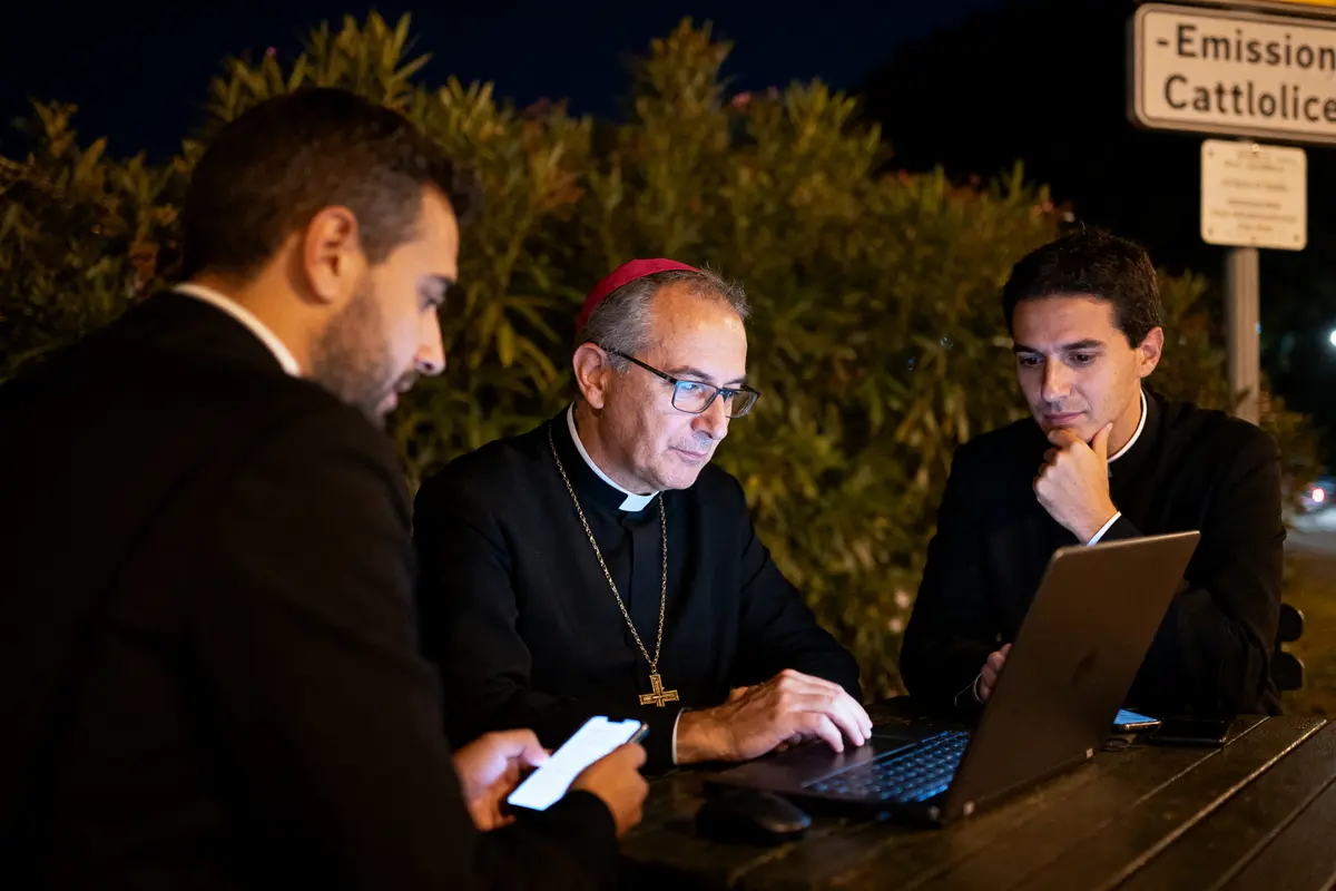 Trois hommes en vêtements religieux consultent un ordinateur et un téléphone à l'extérieur, la nuit.