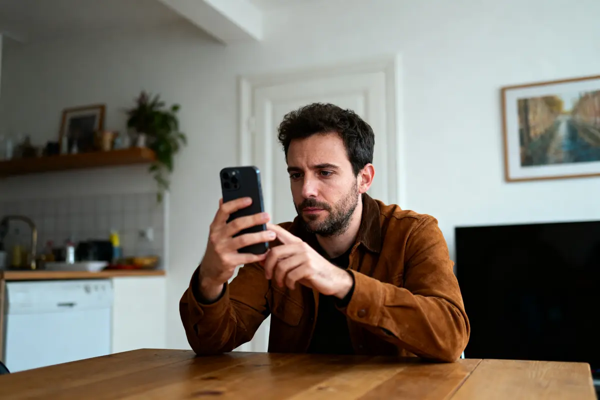 Un homme utilisant un smartphone à table dans une cuisine moderne et lumineuse.