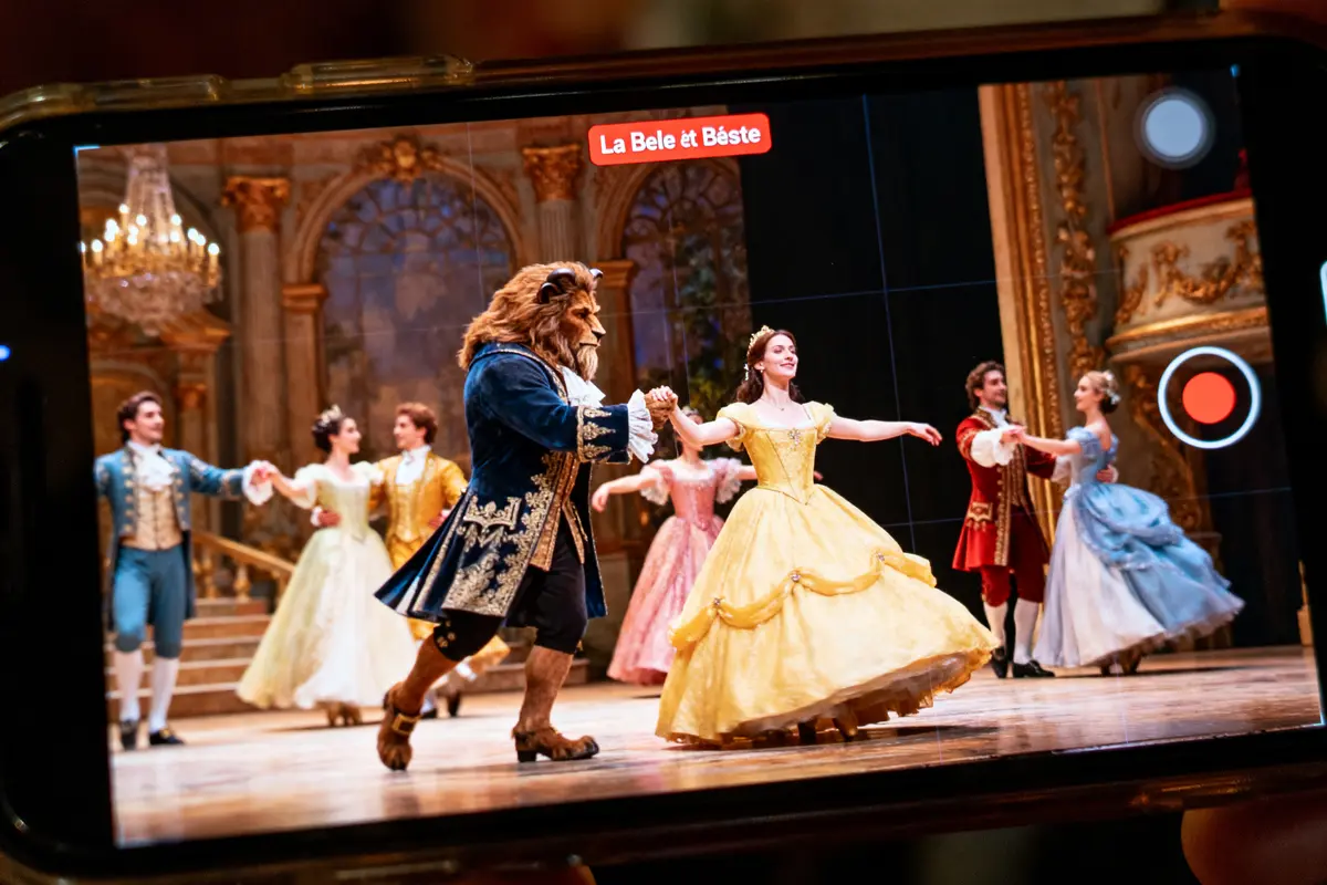 Spectacle "La Belle et la Bête" capturé sur écran de smartphone, personnes en costume sur scène.